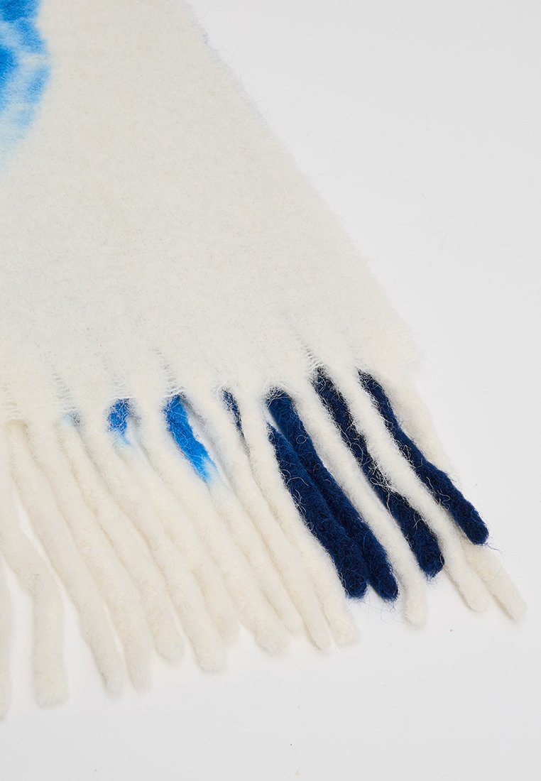 Wollen sjaal in het wit met blauwe en donkerblauwe franjes. Heeft een zachte textuur en een gradientpatroon nabij de bovenkant.