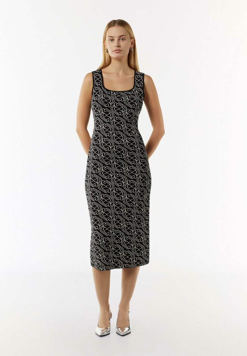 Schwarzes Midi-Kleid mit rechteckigem Ausschnitt, das ein weißes, spiralförmiges Muster aufweist und aus einem glatten Stoff gefertigt ist. Kombiniert mit metallischen High Heels.