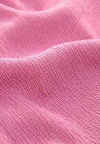 Gestructureerde roze stof met een licht gekreukeld oppervlakpatroon, die subtiele rimpels en een zachte, lichte uitstraling vertoont.