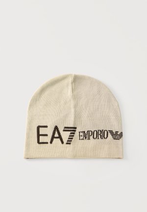 Beżowa dzianinowa czapka z czarnym logo "EA7 Emporio Armani" i symbolem orła z przodu na jasnym tle.