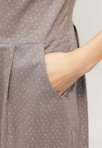 Abito grigio con un sottile motivo bianco, dotato di tasche laterali e una trama di cotone morbida. Il tessuto ha una vestibilità leggermente rilassata.