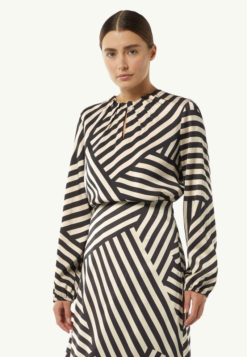 Langärmliges Kleid in Creme mit schwarzen diagonalen Streifen, mit einem Schlüsselloch-Ausschnitt und gerafften Manschetten, aus glattem Stoff gefertigt.