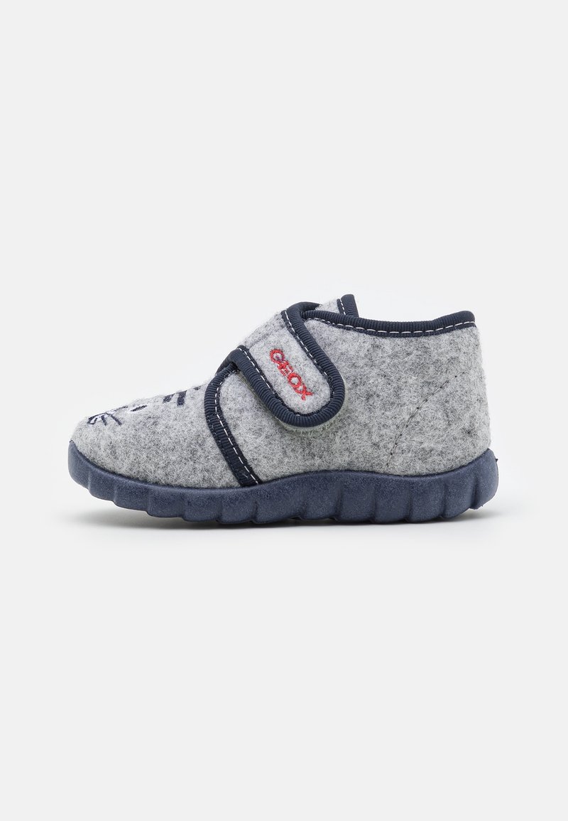 Une chaussure enfant en feutre gris avec semelle marine, bordure marine, bride en velcro et logo rouge sur le côté, vue de profil gauche.