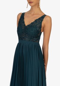Teal formelles Kleid mit V-Ausschnitt, Spitzen-Oberteil mit floralen Stickereien und plissiertem Rock. Leichter Stoff mit transparenten Details.