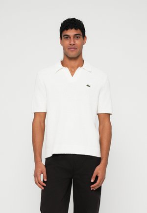 Camisa polo blanca de manga corta con un acabado texturizado y un cuello con muesca. Presenta un pequeño logo verde en el pecho.