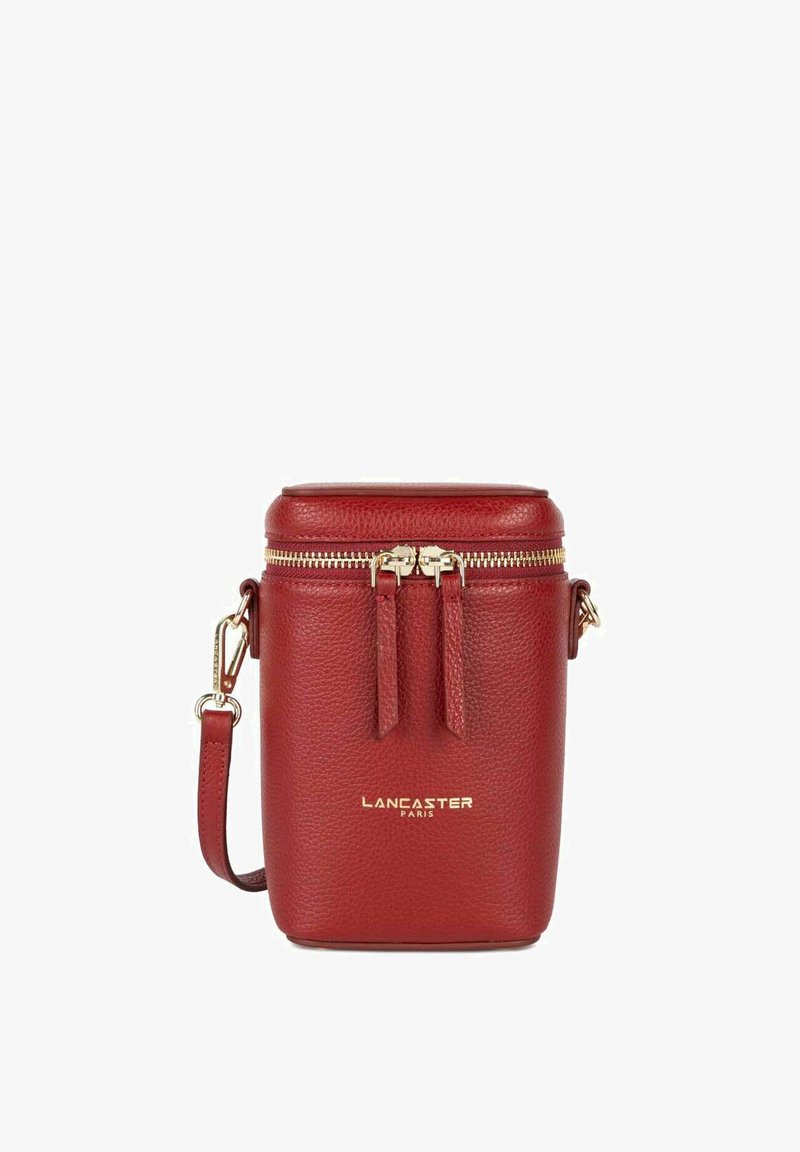 Sac cylindrique en cuir rouge avec quincaillerie dorée, fermeture éclair sur le dessus et deux sangles décoratives. Présente le logo "LANCASTER PARIS" sur l'avant.