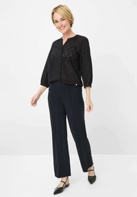 Zwart button-up top met geometrisch uitsnijdpatroon, gecombineerd met marineblauwe wijde broek en zwarte pointed-toe flats. Glad materiaal en relaxte pasvorm.