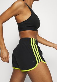 Sujetador deportivo negro y pantalones cortos con vibrantes rayas en neón amarillo. Los pantalones cortos cuentan con una cintura de cordón ajustable y un dobladillo curvado para mayor comodidad y ajuste.