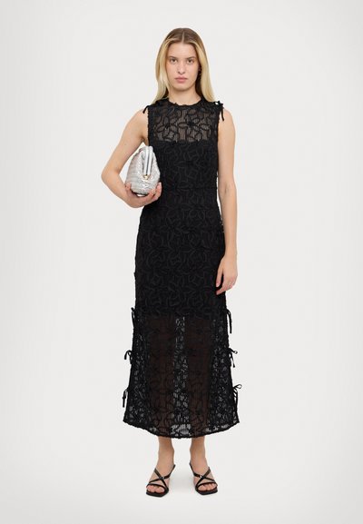 Svart blondekjole med blomstermønster, uten ermer, midt på leggen, og justerbare snorer i kanten. Kombinert med en sølvfarget clutch-veske.