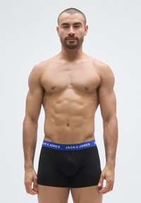 Cuecas boxers pretas de algodão com uma cintura elástica azul que apresenta o texto "JACK & JONES" impresso a branco. Textura lisa, design ajustado.