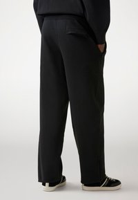 Zwarte trainingsbroek met een relaxte pasvorm, elastische tailleband en twee zijzakken. Gemaakt van zachte stof met een gladde textuur.