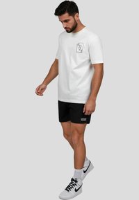 Camiseta de algodón blanca con mangas cortas y un gráfico en el pecho, combinada con pantalones cortos negros con un logotipo y zapatillas blancas.