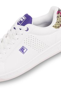 Sneaker bianca con accenti viola, dettagli laterali testurizzati e retro con motivo metallico. Presenta un design tradizionale con lacci e logo.