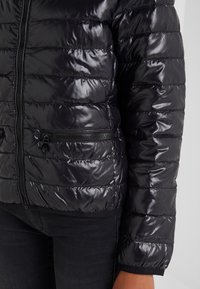 Shiny black puffer jacket with horizontal quilting, zipper pockets, and a close-fitting design. Soft material with flexible hem.