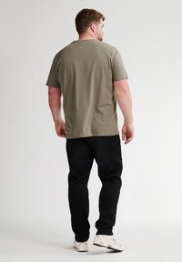 Olivově zelené tričko s krátkým rukávem a kulatým výstřihem v kombinaci s černými kalhotami a bílými teniskami. Jednoduchý design, měkká látka, volný střih.