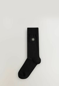 Sort bomuldssok med ribbet manchet og et let broderet cirkulært mønster med røde, hvide og grønne accenter på siden.