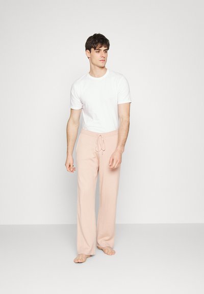 Calças de lounge rosa claro com cintura elástica, combinadas com uma t-shirt branca ajustada. Tecido suave, ajuste relaxado e design de perna reta.