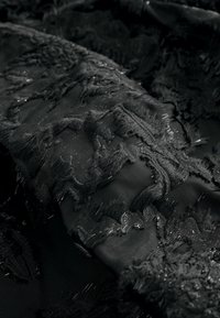 Mustmust kangas, millel on tekstuurne tikand fraktsioonide servadega ja õrnade metallniitidega, mis lisavad detaili. Sile aluskate on nähtav.