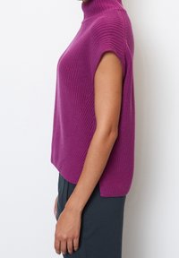 Fuksjowy dzianinowy top z wysokim kołnierzem i krótkimi rękawami. Charakteryzuje się fakturowanym wzorem, luźnym krojem i delikatnym skośnym wykończeniem na bokach.