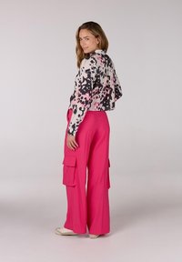 Korte witte blouse met zwarte en roze spetterpatronen, gecombineerd met hoge roze cargobroeken met zijzakken.