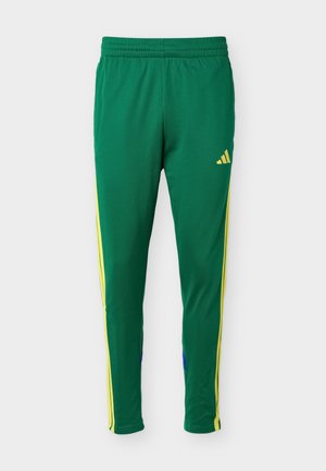 Groene sportbroek met gele zijstrepen en elastische tailleband, voorzien van een klein geel Adidas-logo op de rechterdij.