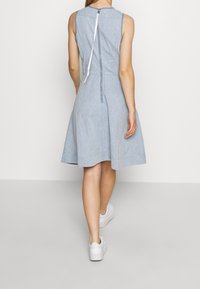 Ljusblå chambrayklänning med utsvängd kjol, ärmlös design, dragkedjestängning i ryggen och en slät yta. Bärs med vita sneakers.