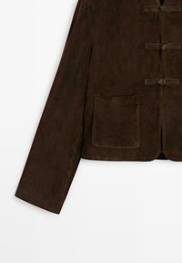 Manche de veste en daim marron foncé avec poche plaquée avant et trois fermetures à bascule horizontales sur fond blanc.