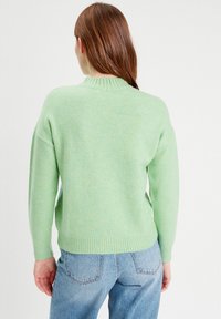 Lys grøn strikket sweater med ribbet halsudskæring og manchetter. Sweateren har dropped shoulders og en afslappet pasform, som er parret med lyseblå jeans.