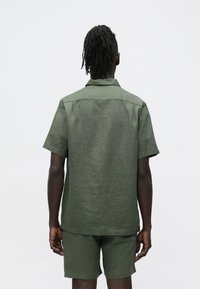 Korte mouw, olijfgroen overhemd van linnen; heeft een klassieke kraag en een losse pasvorm met een gestructureerd oppervlak.