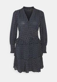 Marinblå klänning med långa ärmar, V-ringning och elastisk midja. Har en volangslå och ett vitt prickigt mönster. Lätt, flödande tyg.