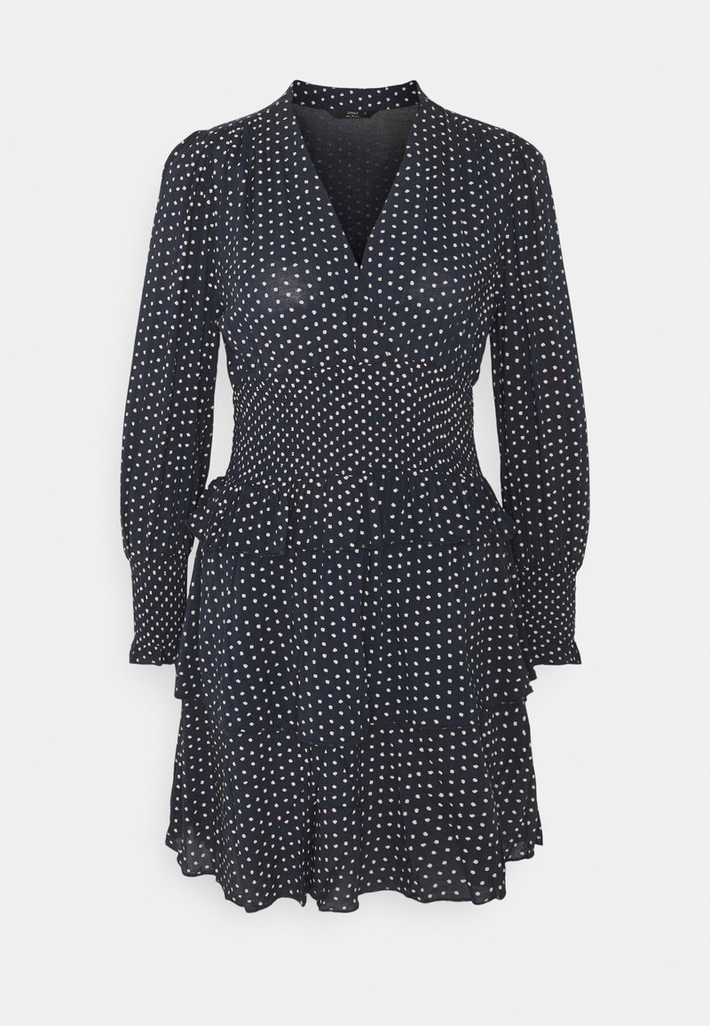 Marinblå klänning med långa ärmar, V-ringning och elastisk midja. Har en volangslå och ett vitt prickigt mönster. Lätt, flödande tyg.