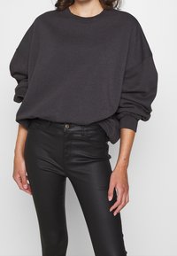 Kolgrå oversized sweatshirt med sänkta axlar och ribbade ärmar, kombinerad med svarta åtsittande läderbyxor som har en snygg yta.