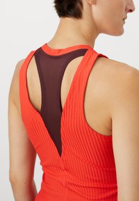 Rotes Sporttop mit vertikaler gerippter Textur, das über einen tiefen V-förmigen Rückenausschnitt und ein kontrastierendes dunkles Netzpaneel verfügt.