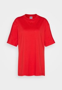 Červené tričko s krátkým rukávem vyrobené z bavlny, s kulatým výstřihem, volným střihem a jemným logem na přední straně. Hladká textura.