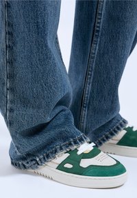 Groene en witte sneakers met perforaties en suède accenten, gecombineerd met vervaagde blauwe wijde denim jeans met rafelige zoom.