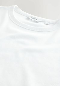Tricou alb cu dungi, având un guler rotund, material ușor texturat și un model subtil de dungi. Eticheta de marcă "NEXT" pe gulerul interior.