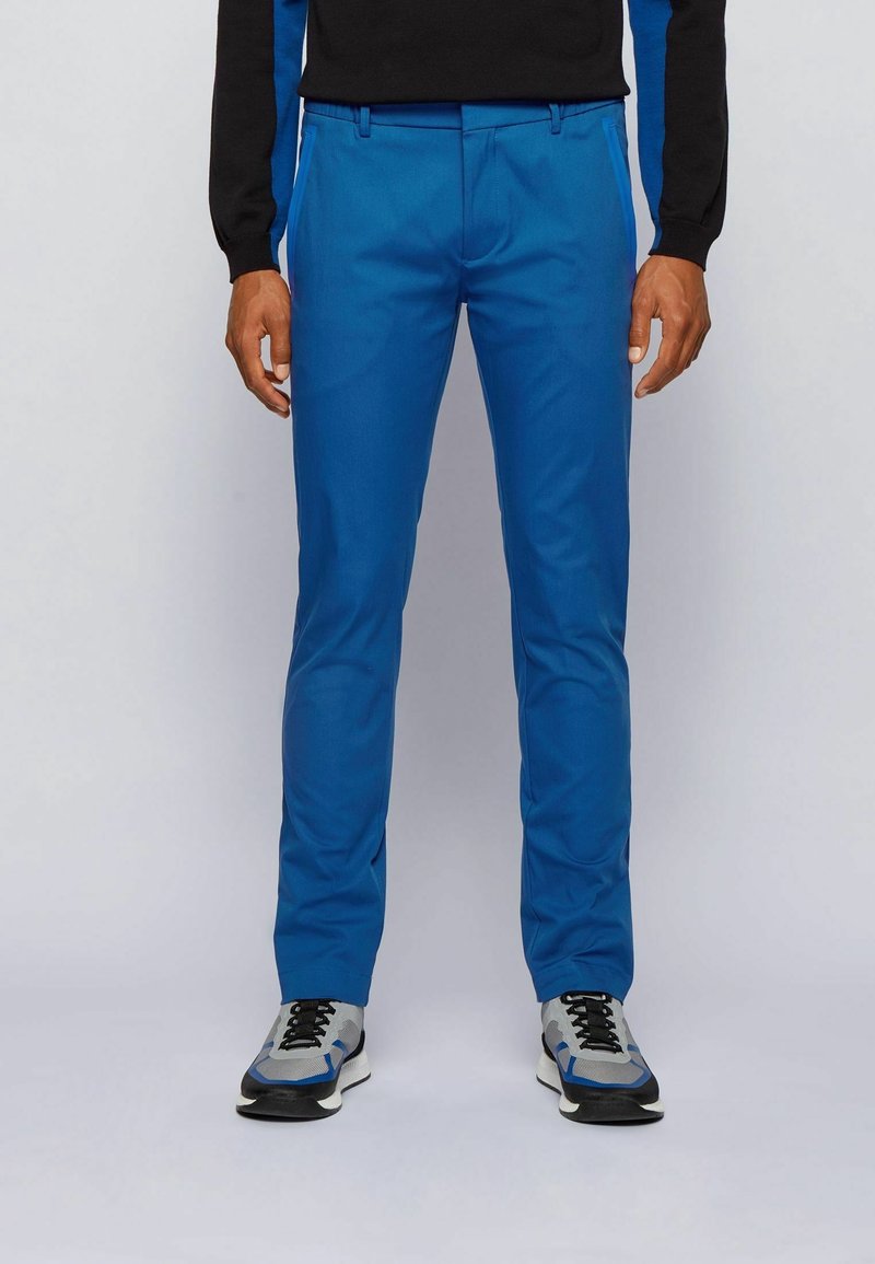 Blå slim-fit byxor gjorda av ett slätt tyg, med bältesöglor, sidofickor och en veck fram. Matchas med grå sneakers.