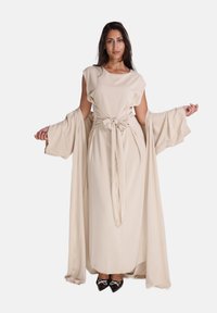 Beige lange jurk met een geaccentueerde taille, vloeiende mouwen en een strikceintuur. Heeft een eenvoudig, elegant ontwerp met een zachte textuur en draping.