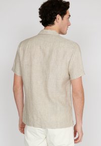 Camicia beige a maniche corte realizzata in lino tessurizzato, con inserti posteriori e orlo dritto. Design leggero e informale, adatto per climi caldi.