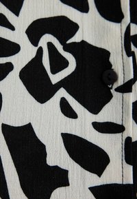 Black and white floral patterned fabric with a smooth texture, featuring a black button detail and visible stitching along the edge.