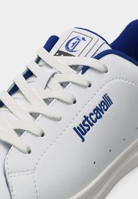 Λευκό αθλητικό παπούτσι με μπλε λεπτομέρειες, λευκά κορδόνια, κεντημένο λογότυπο «Just Cavalli» στο πλάι και ετικέτα με τη μάρκα στη γλώσσα.