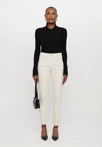 Black ribbed long-sleeve button-up shirt paired with high-waisted white jeans and black pointed-toe heels, carrying a small black handbag.
