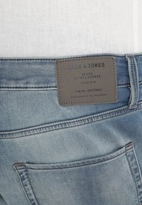Jeans in denim blu con una patch in pelle sul retro che presenta testo in rilievo e una tasca posteriore con doppia cucitura e una leggera sfumatura.