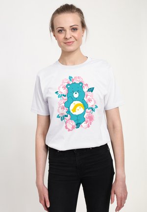 Hvid bomulds t-shirt med en blå bjørn illustration omgivet af lyserøde roser, med et gult sols designs på bjørnens mave.