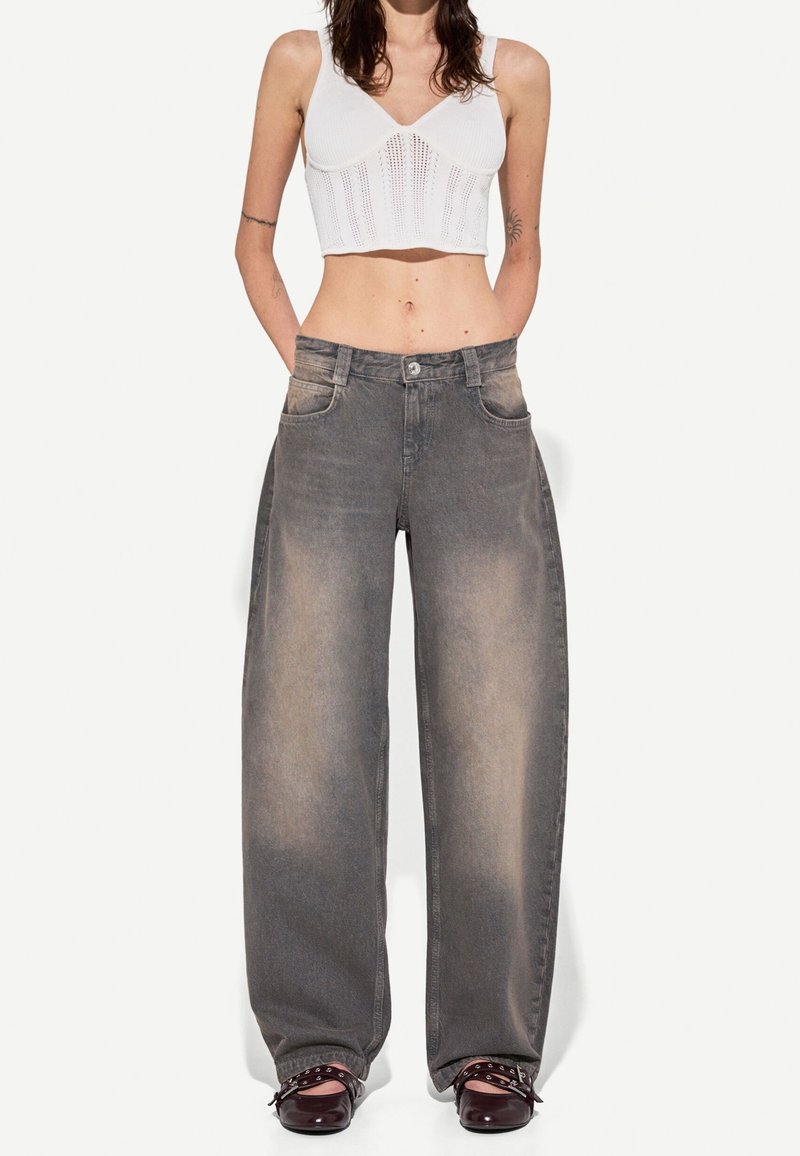 Vida vida, grå jeans med vida ben, som är urblekta, med två framfickor och knäppning, i kombination med en kort vit topp. Slät textur, avslappnad design.