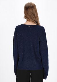 Navy blue sweter, luźny krój, teksturowany splot z subtelnymi błyskami, szerokim dekoltem, opadającymi ramionami oraz ściągaczami u dołu i na mankietach.