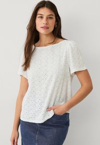 Hvid kortærmet top med hulmønster, rund halsudskæring og afslappet pasform. Tekstureret stof, parret med en denim nederdel.