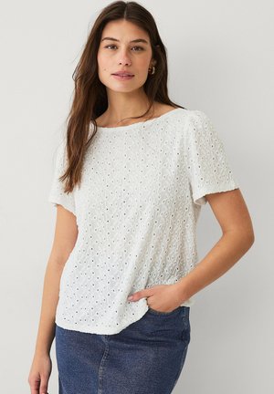 Haut blanc à manches courtes avec motif œillet, encolure ronde et coupe décontractée. Tissu texturé, associé à une jupe en denim.