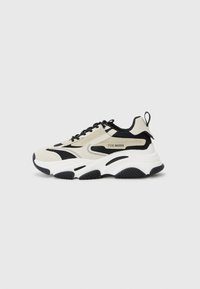 Chunky sneaker with a beige and black mesh upper, white midsole, black rubber outsole, and logo detailing on the side.