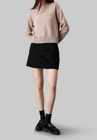 Jasnoróżowy dzianinowy sweter z prążkowanym stanem, zestawiony z czarną dżinsową mini spódnicą. Czarne buty na grubym podbiciu i skarpetki.